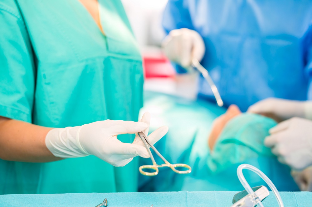 Hospital - Surgery Team In The Operating Room Or Op Of A Clinic Operating On A Patient, Perhaps It's An Emergency A Assistant Holding A Cotton Swap Forceps